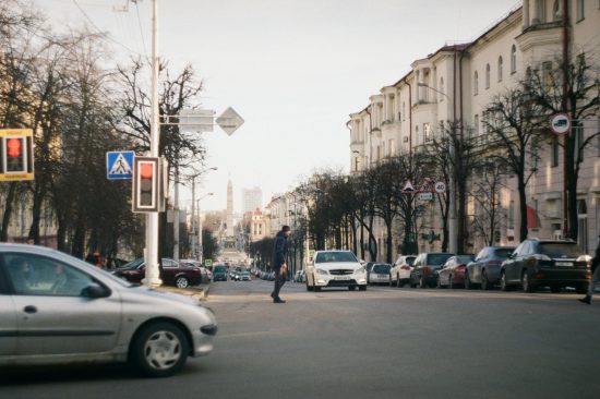 Street view of an urban crossing in Minsk with vehicles and a pedestrian.